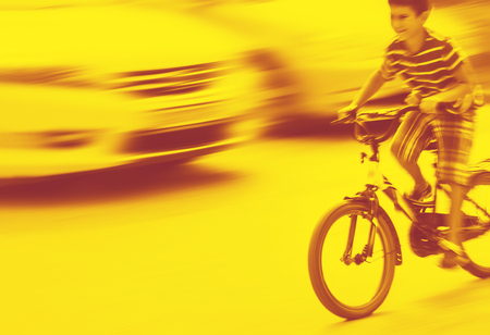 Duotone yellow and red image of dangerous city traffic situation with a boy on bicycle and cars in motion blurの写真素材