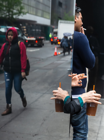 New York, USA - May 03, 2016: Coffee break in the streets of New York City. Hand of a woman with a cup of coffee and the hand of a man with a cigarette reflected in a glass caseのeditorial素材