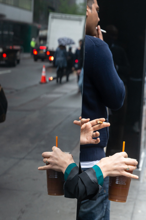 New York, USA - May 03, 2016: Coffee break in the streets of New York City. Hand of a woman with a cup of coffee and the hand of a man with a cigarette reflected in a glass caseのeditorial素材