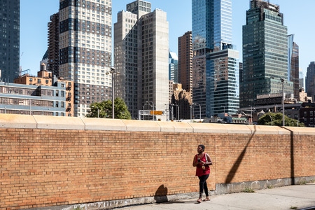 New York, USA - Sep 23, 2017: Manhattan street scene. Black young woman with a mobile phone walk along a yellow brick fence on the streets of Manhattan in New York Cityのeditorial素材