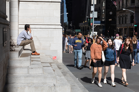 NEW YORK, USA - Sep 23, 2017: Manhattan street scene. Man is sitting on the steps of Saint Thomas Church Fifth Avenue. New Yorkers and tourists in a hurry about their business, walking on Fifth Avenueのeditorial素材