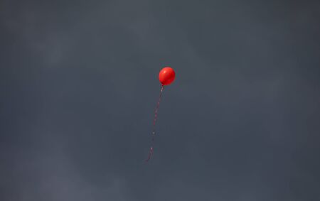 Red helium balloon against the grey sky backgroundの写真素材
