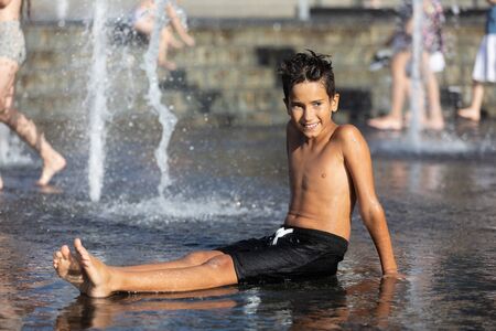 11 years old happy boy playing in a water fountain and enjoying the cool streams of water in a hot day. Hot summer.の写真素材