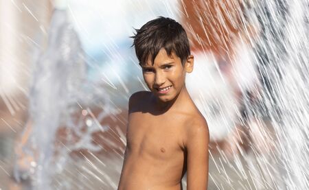 11 years old happy boy playing in a water fountain and enjoying the cool streams of water in a hot day. Hot summer.の写真素材