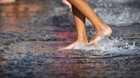 Happy children playing in a water fountain in a hot day. Close-up of children legs in a fountainの写真素材