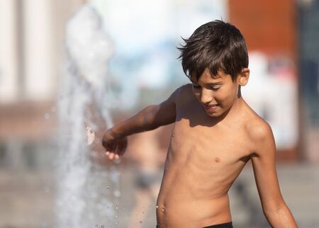 11 years old happy boy playing in a water fountain and enjoying the cool streams of water in a hot day. Hot summer.の写真素材