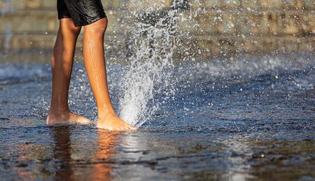Happy children playing in a water fountain in a hot day. Close-up of children legs in a fountainの写真素材