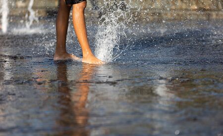 Happy children playing in a water fountain in a hot day. Close-up of children legs in a fountainの写真素材