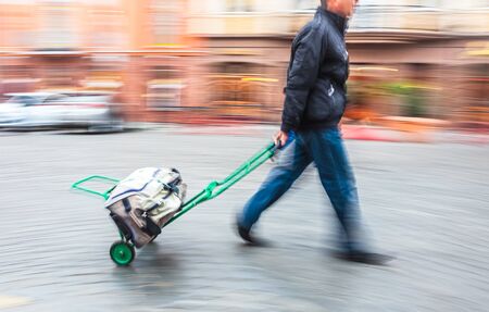 Middle-aged man carries the cart with bag. Intentional motion blur