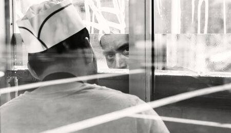NEW YORK, USA - Apr 28, 2016: Manhattan street scene. Portrait of a seller at a fast food kiosk in Manhattan. The face is reflected in the mirror. Black and white imageのeditorial素材