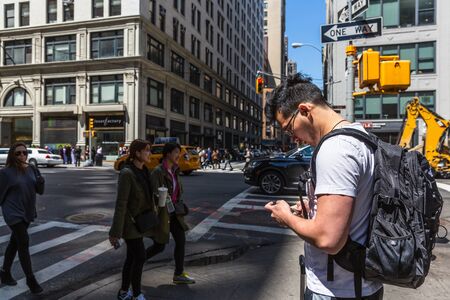 NEW YORK, USA - Apr 30, 2016: Manhattan street scene. The Americans on the streets of New York City. Young man with a backpack looks at a mobile phoneのeditorial素材