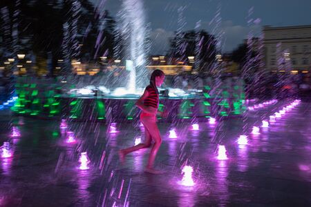 LUBLIN, POLAND - JULY 27, 2018: Happy children playing in a water fountain in Lublin at night. Lublin is the ninth largest city in Polandのeditorial素材
