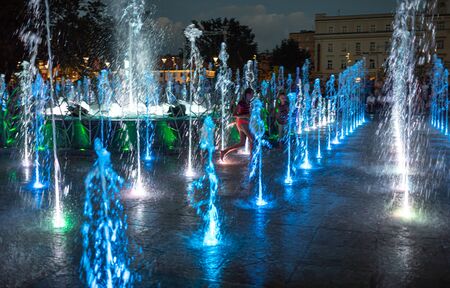 LUBLIN, POLAND - JULY 27, 2018: Happy children playing in a water fountain in Lublin at night. Lublin is the ninth largest city in Polandのeditorial素材