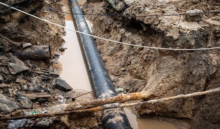 Repair of roads and underground utilities. Big trench on the road with a pipe, the process of repair or replacing of water pipes in big city. Ð¡onstruction and repair of underground waterの写真素材