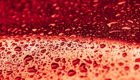 Rain drops on a red surface. Water drops on red metal texture. Shallow focus. Detail of red wet...