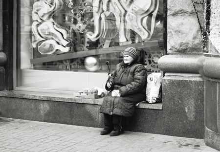 Kyiv, Ukraine - Nov 16, 2019: Disadvantaged and impoverished people on the street of Kiev. An elderly woman sits near a shop window and sells nuts and a decorative flower.のeditorial素材