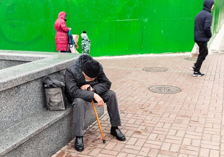 Kyiv, Ukraine - Nov 16, 2019: Disadvantaged and impoverished people on the street of Kiev. An elderly tired man sits on a granite slab. Homeless old manのeditorial素材
