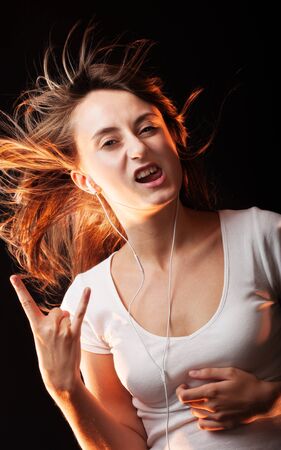 Beautiful Woman Listening Music. Attractive smiling happy woman dancing and listening to music in headphone on dark studio background, wearing white shirt. Flying hair and having fun.の写真素材
