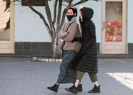 Uzhgorod, Ukraine - Apr. 10, 2020: People in medical masks on the street rush about their business during the coronavirus epidemic. Two young womenのeditorial素材
