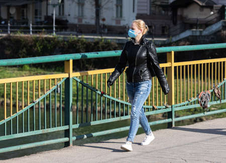 Uzhgorod, Ukraine - Apr. 10, 2020: People in medical masks on the street rush about their business during the coronavirus epidemic. Young womanのeditorial素材