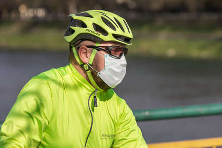 Uzhgorod, Ukraine - Apr. 10, 2020: People in medical masks on the street rush about their business during the coronavirus epidemic. Young man in sportswear and a protective helmetのeditorial素材