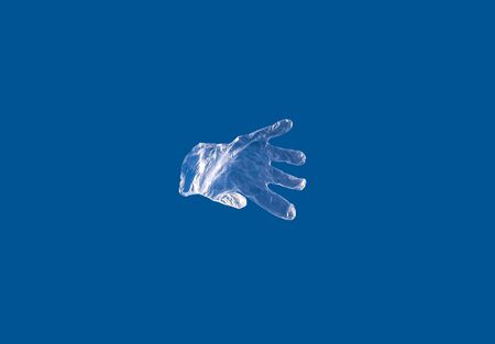 A disposable plastic glove flies against a blue sky during a coronavirus epidemicの写真素材