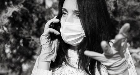 Young woman in a medical mask with a mobile phone emotionally communicates and gesturesの写真素材