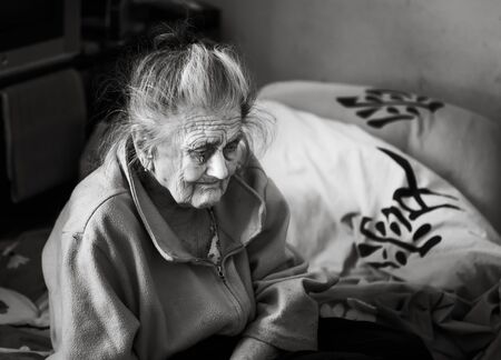 Old age concept. Portrait of a very old and tired of life wrinkled woman near the window in the...