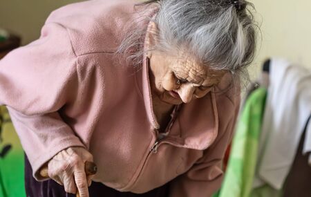 Old age concept. Portrait of a very old and tired of life wrinkled woman near the window in the bedroom of her house. Sad and depressed older woman aloneの写真素材