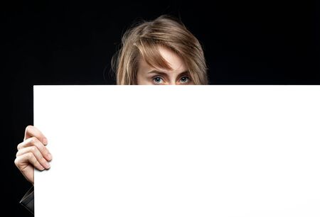 Teenage girl with an empty board for advertising and announcements. Fashion, portrait and people concept. Portrait of a young emotional woman on a dark backgroundの写真素材