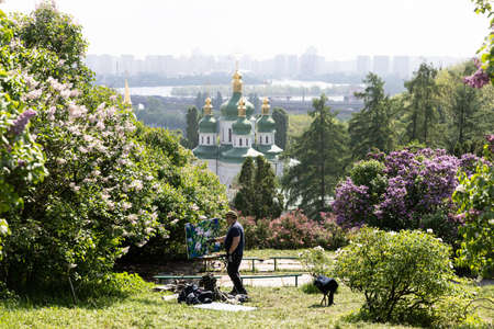 KYIV, UKRAINE - May 10, 2019: View of Vydubychi Monastery, Dnipro river and lilac flowers in Hryshko National Botanical Garden in Kyiv. The artist paints flowering treesのeditorial素材