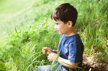 Happy lifestyle concept. Little boy sits on a bench in the park and plays with a mobile phoneの写真素材