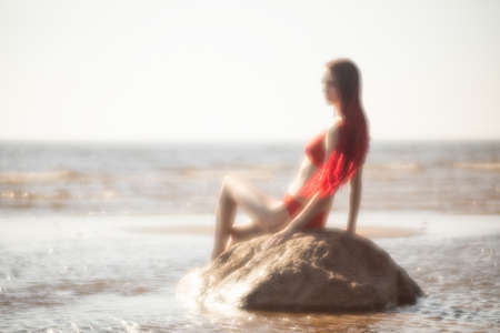 Soft focus blurred image of a beautiful young woman with scarlet dreadlocks and red bathing suit enjoying nature on the beachの写真素材