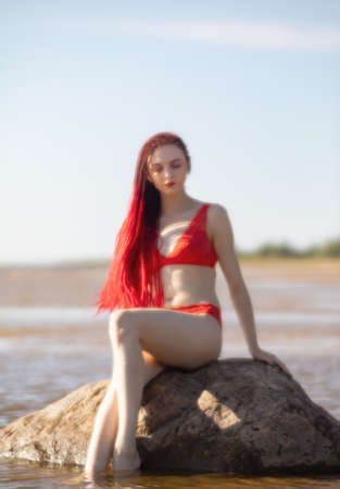 Soft focus blurred image of a beautiful young woman with scarlet dreadlocks and red bathing suit enjoying nature on the beachの写真素材