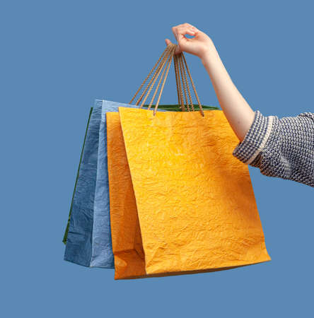 Hand holds colored paper shopping bags on blue backgroundの写真素材