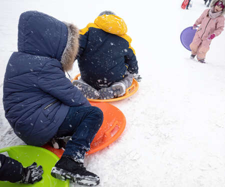 KYIV, UKRAINE - Jan. 30, 2021: Outdoor winter fun. Children sledding and snowboarding in a big city after a snowfall. Active winter outdoors games. Everything is covered with snow aroundのeditorial素材