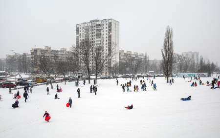 KYIV, UKRAINE - Jan. 30, 2021: Outdoor winter fun. Children sledding and snowboarding in a big city...
