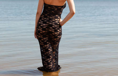 Young red-haired woman in a black lace dress on a naked body posing on the seashoreの写真素材