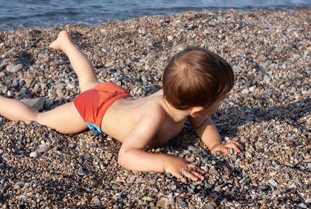 Healthy lifestyle. Little boy resting lying on the stones on the rocky beach on the Mediterranean seaの写真素材