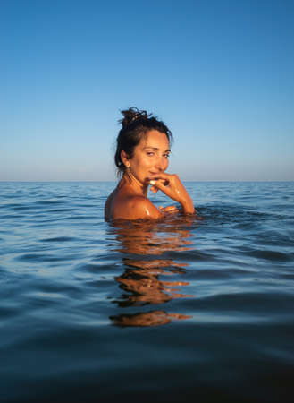 Relaxation and healthy lifestyle. Young beautiful and emotional woman swims in the sea on a sunny day. Portrait in sea waterの写真素材