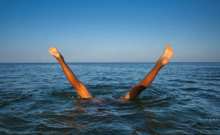 Relaxation and healthy lifestyle. Young boy teenager bathes in the sea. The boy dives and his legs...