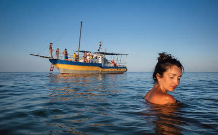 Relaxation and healthy lifestyle. Young beautiful and emotional woman swims in the sea on a sunny day. Boat in the backgroundの写真素材