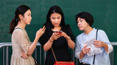 NEW YORK, USA - Sep 17, 2017: Three asian women standing against green wall and looking for information by using smartphones and advertising booklets on the streets of Manhattan in New Yorkのeditorial素材