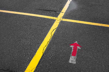 Dark wet asphalt with puddle, with yellow markings in the form of a crosshair of two lines and a white and red directional arrowの写真素材