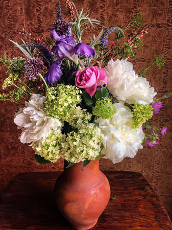 Spring bouquet of farm flowers in the interior. Floristics - art of flowers arrangements. Romantic bouquet with rose, peonies, iris, hydrangea, allium, parsley blossoms, wormwood leaves, geyhera, veronicaの写真素材