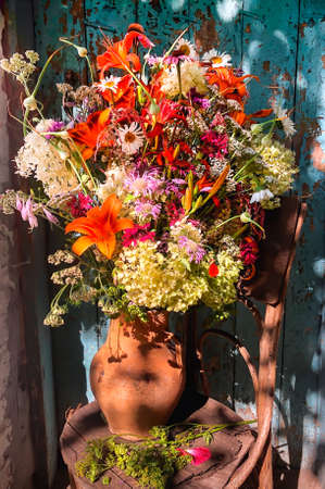Romantic bouquet with daylilies, echinocea, monarda, hydrangea, yarrow, hosta, chamomile, parsnip and garlic in a retro style in the courtyard against the background of a blue old doorの写真素材