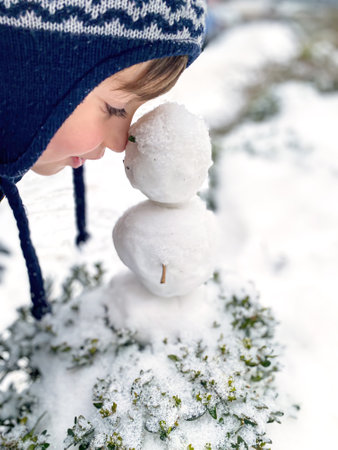 Portrait of a happy five year old boy in the snow in winter. The boy plays and poses with a little snowmanの写真素材