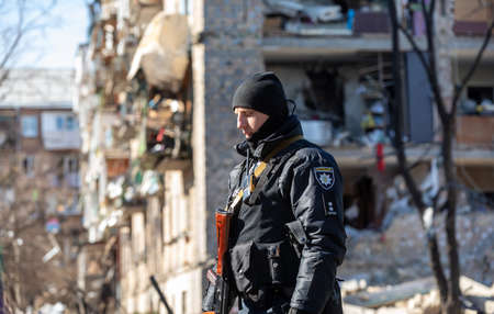 KYIV, UKRAINE - Mar. 18, 2022: War in Ukraine. Damaged residential buildings in the aftermath of a shelling in Podilskyi district of Kyiv. A policeman guards the order near the destroyed houseのeditorial素材