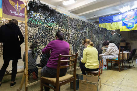 KYIV, UKRAINE - Apr. 01, 2022: A group of volunteers in a shelter making camouflage net, from...