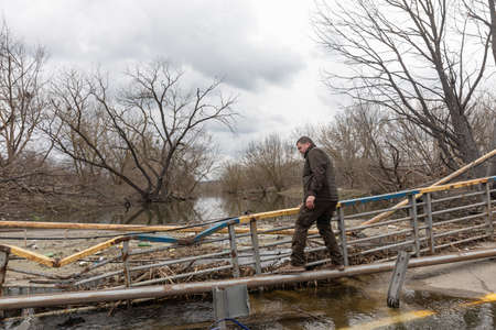 IRPIN, UKRAINE - Apr. 10, 2022: Man cross the Irpin river near a destroyed bridge outside the liberated Irpin townのeditorial素材